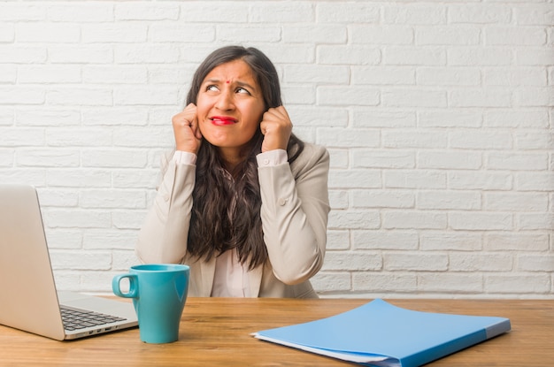 Young indian woman at the office covering ears with hands, angry and tired of hearing some sound