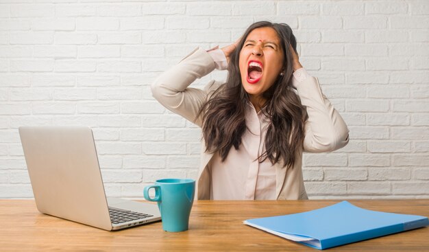 Young indian woman at the office crazy and desperate, screaming out of control, funny lunatic expressing freedom and wild