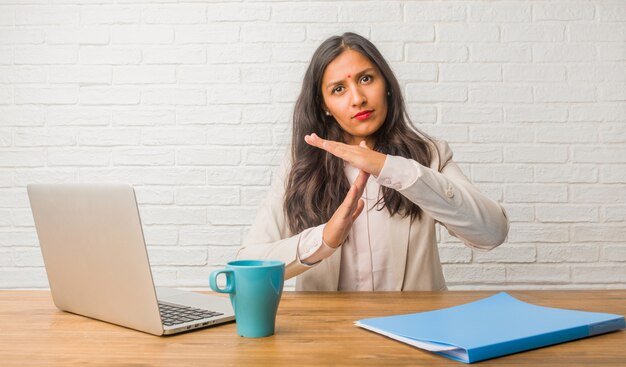 Young indian woman at the office tired and bored, making a timeout gesture