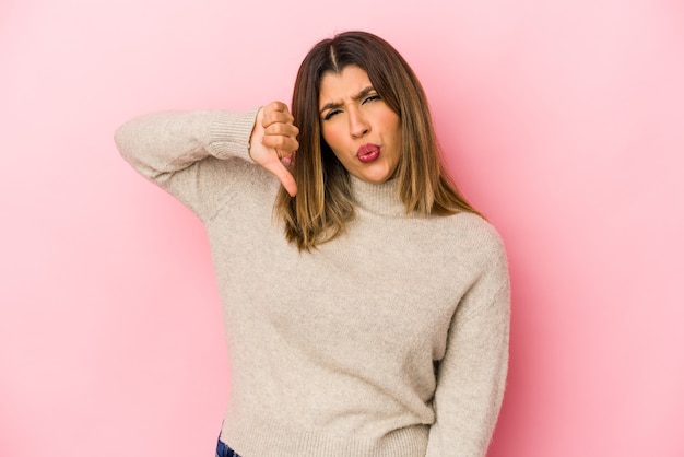 Young indian woman on pink showing thumb down and expressing dislike.