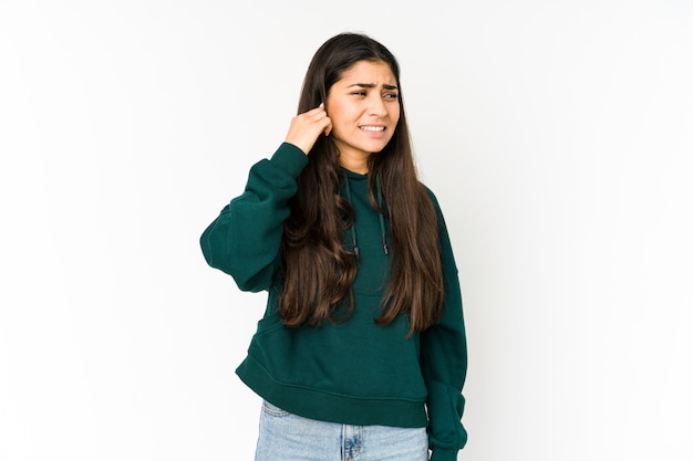 Young indian woman on purple wall covering ears with hands.