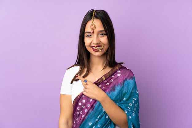 Young indian woman on purple wall pointing to the side