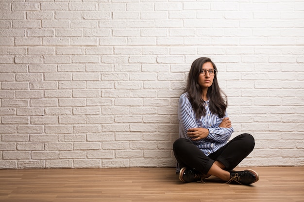 Young indian woman sit against a brick wall crossing his arms, serious and imposing