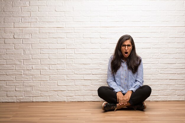 Young indian woman sit against a brick wall very angry and upset, very tense, screaming fu