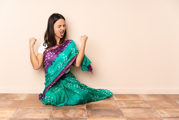 Foto giovane donna indiana seduta sul pavimento facendo un gesto forte