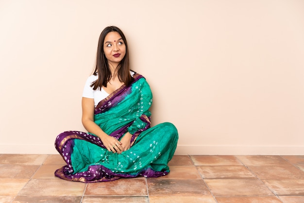 Young Indian woman sitting on the floor having doubts while looking side