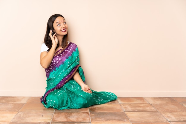誰かと携帯電話で会話をしながら床に座っている若いインド人女性