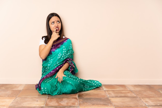 Young Indian woman sitting on the floor nervous and scared