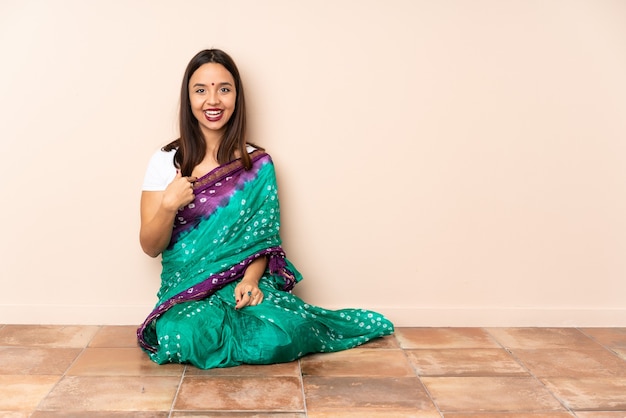 Young Indian woman sitting on the floor with surprise facial expression