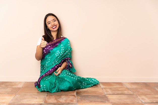 Young Indian woman sitting on the floor with thumbs up because something good has happened