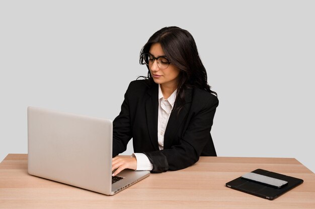 Young indian woman in a table with a laptop and tablet using a mobile phone isolated