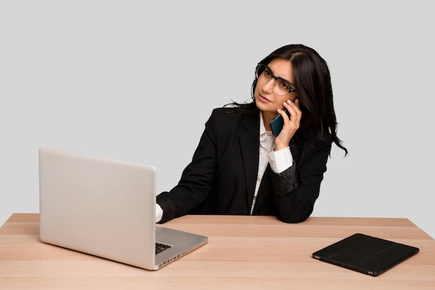 Young indian woman in a table with a laptop and tablet using a mobile phone isolated