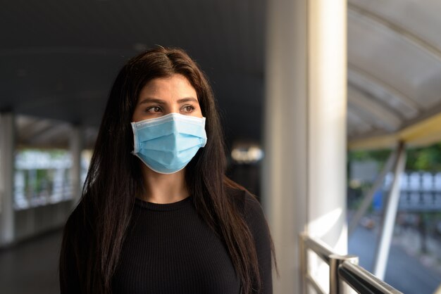 Giovane donna indiana pensando con maschera per la protezione dall'epidemia di virus corona presso la passerella