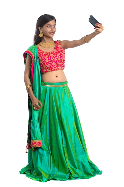 Young Indian woman using a mobile phone or smartphone, talking selfie or talking on video chat isolated on a white wall