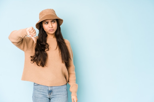 Young indian woman wearing a hat showing thumb down and expressing dislike.