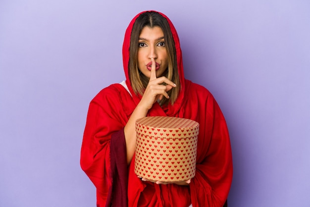 Young indian woman wearing a hijab holding a valentines day gift isolated keeping a secret or asking for silence.