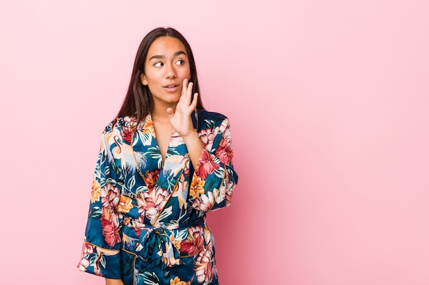 Young indian woman wearing a kimono pajama is saying a secret hot braking news and looking aside