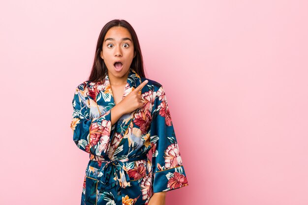 Young indian woman wearing a kimono pajama pointing to the side