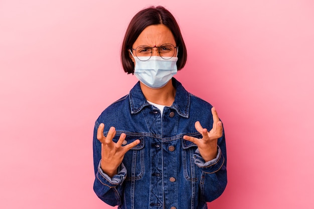 Young Indian woman wearing a mask antivirus isolated on pink background upset screaming with tense hands.