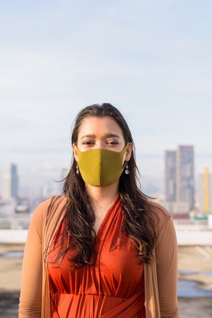 Young Indian woman wearing mask for protection from corona virus outbreak against view of the city