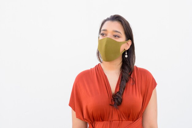 Young Indian woman wearing mask and thinking against white background