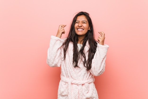 Young indian woman wearing pajama crossing fingers for having luck