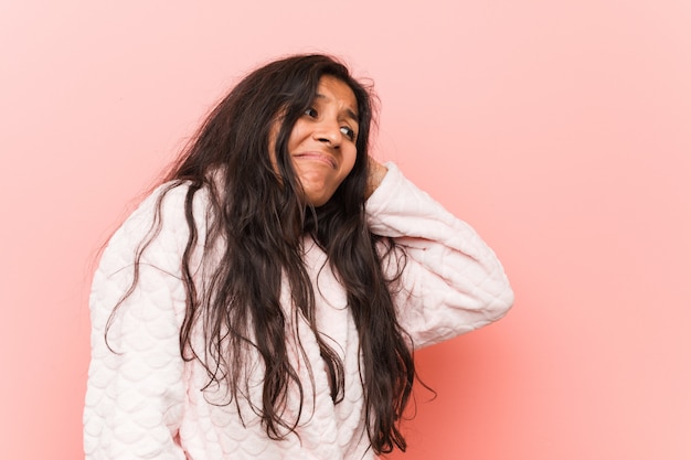 Young indian woman wearing pajama touching back of head, thinking and making a choice.