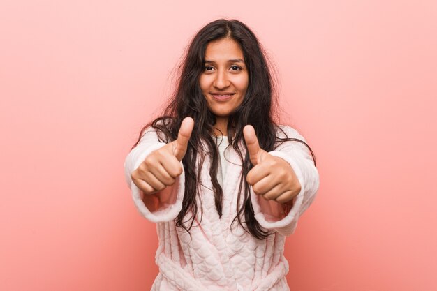Молодая индийская женщина в пижаме с большими пальцами руки вверх, приветствует что-то, поддерживает и уважает концепцию.