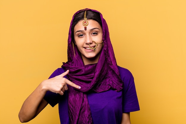 Young Indian woman wearing a traditional sari clothes isolated on yellow wall person pointing by hand to a shirt copy space, proud and confident