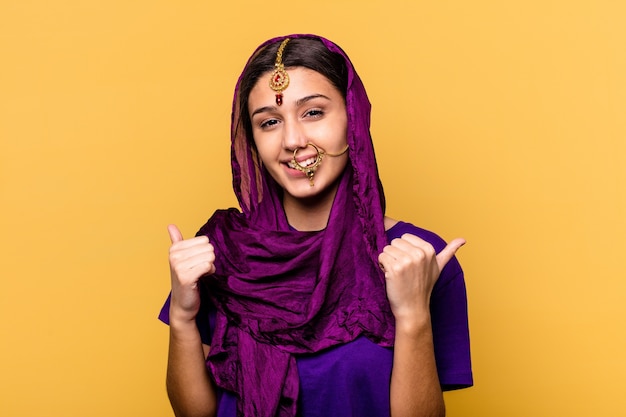 Young Indian woman wearing a traditional sari clothes isolated on yellow wall raising both thumbs up, smiling and confident