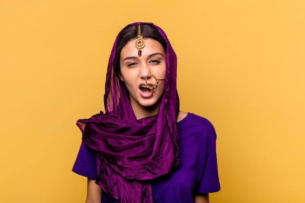 Young Indian woman wearing a traditional sari clothes isolated on yellow wall screaming very angry and aggressive