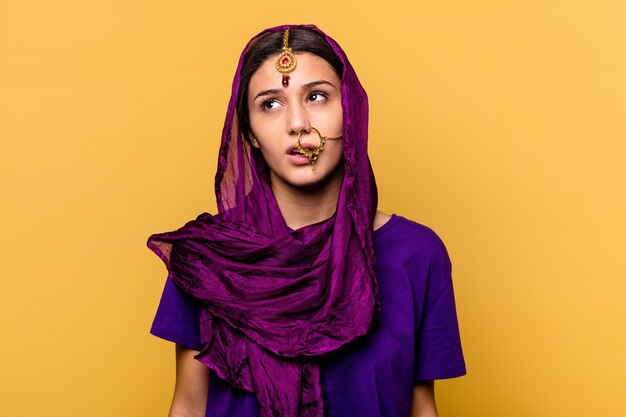 Young Indian woman wearing a traditional sari clothes isolated on yellow wall tired of a repetitive task