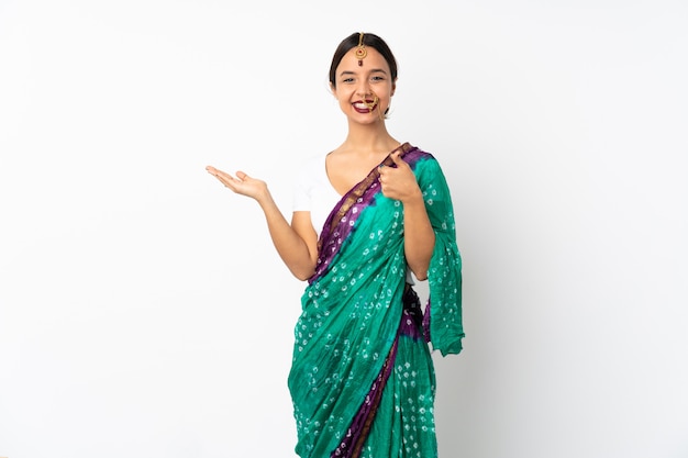 Young indian woman on white wall holding blank space on the palm and with thumbs up