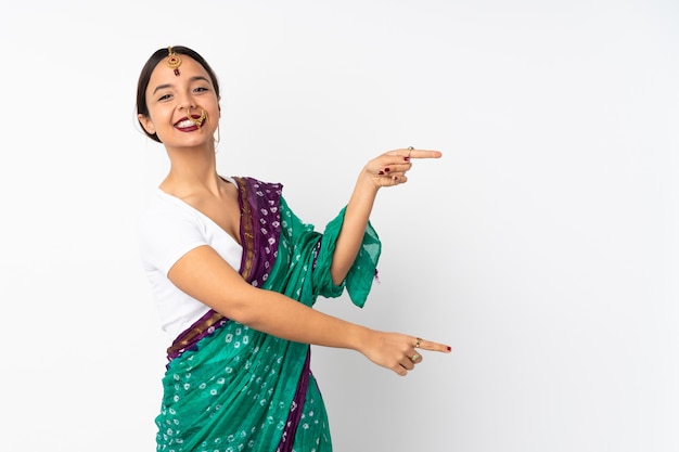 Young indian woman on white wall pointing finger to the side and presenting a product