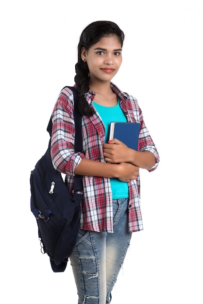 Young Indian woman with backpack standing and holding notebooks, posing on a white wall.