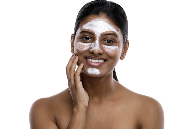 Young indian woman with a cleansing mask applied on her face. Isolated on white.