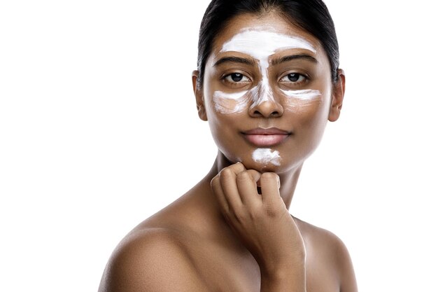 Giovane donna indiana con una maschera detergente applicata sul viso su sfondo bianco.