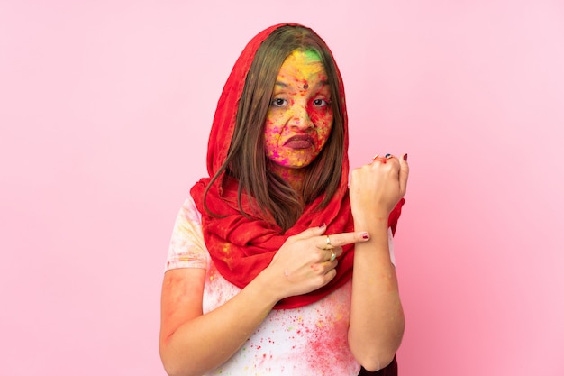 Young Indian woman with colorful holi powders on her face isolated on pink wall making the gesture of being late