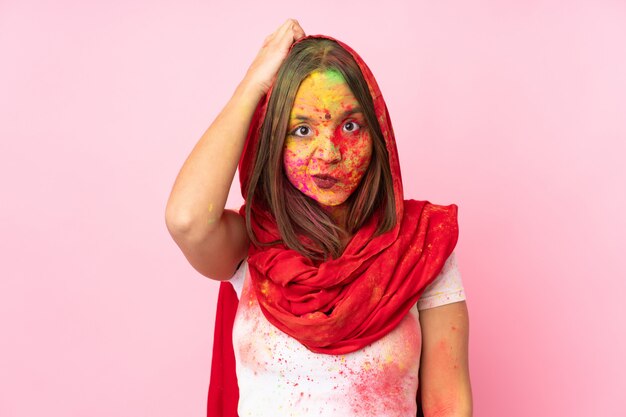 Молодая индийская женщина с красочными порошками Холи на лице, изолированные на розовой стене с выражением разочарования и непонимания