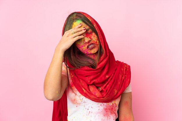 피곤하고 아픈 표정으로 분홍색 벽에 고립 된 그녀의 얼굴에 화려한 holi 분말을 가진 젊은 인도 여자