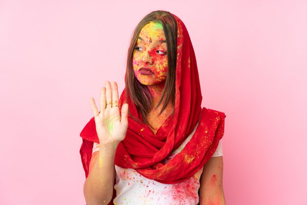 Young Indian woman with colorful holi powders on her face isolated on pink wall