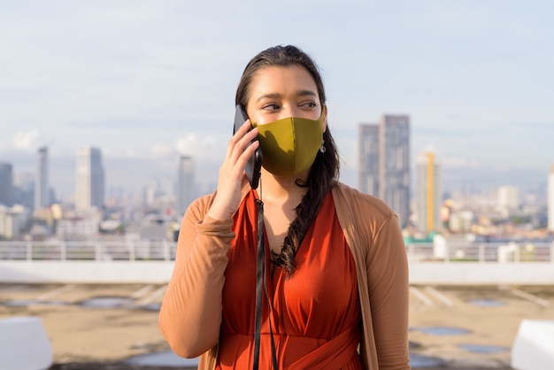 Foto giovane donna indiana con la maschera che parla sul telefono contro la vista della città