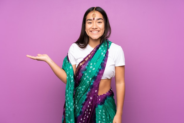 Young indian woman with sari over isolated background holding\
copyspace imaginary on the palm to insert an ad