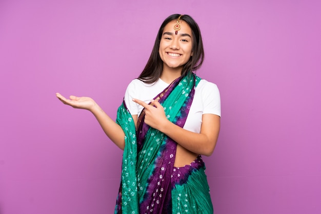 Young Indian woman with sari over isolated wall holding copyspace imaginary on the palm to insert an ad