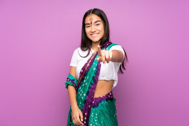 孤立した壁の上のサリーと若いインド人女性は自信を持って表現で指を指す