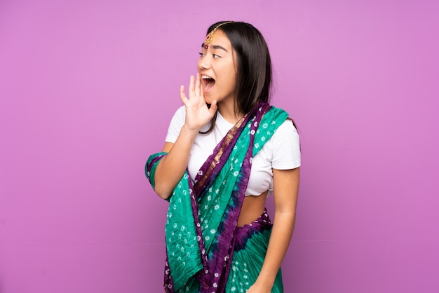 Young Indian woman with sari over wall shouting with mouth wide open to the side
