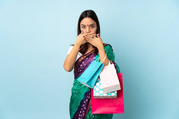 Young Indian woman with shopping bags covering mouth with hands