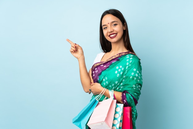 Young Indian woman with shopping bags pointing finger to the side