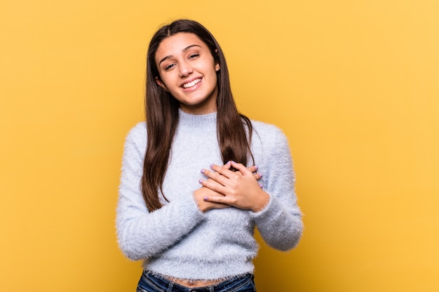 Young Indian woman on yellow laughing keeping hands on heart, concept of happiness.