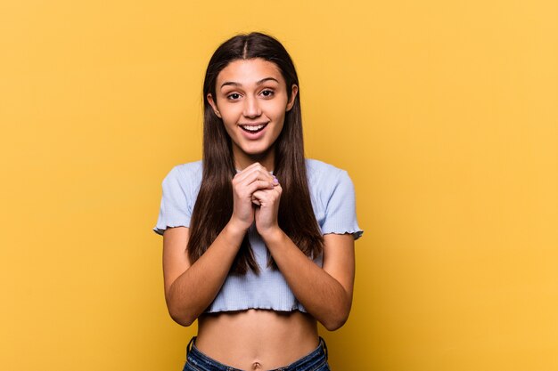 Young Indian woman on yellow praying for luck, amazed and opening mouth looking to front.